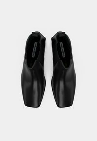 Ζευγάρι μαύρων δερμάτινων παπουτσιών slip-on με τετράγωνη μύτη, ελαστικές πλευρές και επώνυμες σόλες σε λευκό φόντο.