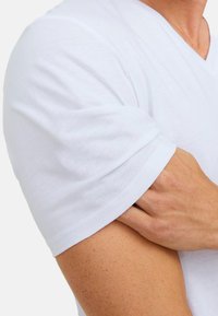 Hvid bomulds T-shirt med V-halsdesign og korte ærmer, der viser en glat tekstur og en tætsiddende stil.