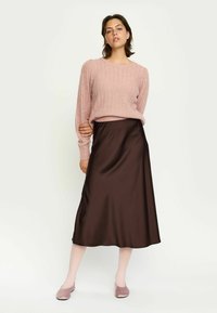 Lichtroze geribbelde gebreide trui gecombineerd met een bruine satijnen midi rok. De outfit heeft een ontspannen pasvorm en een soepele textuur, met roze schoeisel.