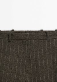 Pantalon en laine marron foncé avec de fines rayures blanches verticales et passants de ceinture visibles le long de la ceinture.