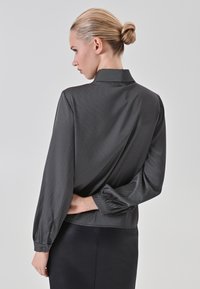 Blusa a strisce bianco e nere con maniche lunghe e gonfiate e colletto alto, caratterizzata da una texture liscia e un design aderente in vita.