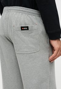 Gros plan d'une personne portant un pantalon de survêtement gris avec une ceinture élastique et une poche arrière marquée Diesel.