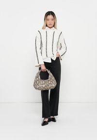 Knit white sweater with black vertical lines, paired with black trousers and a snake-print handbag. Model holds bag with one hand.