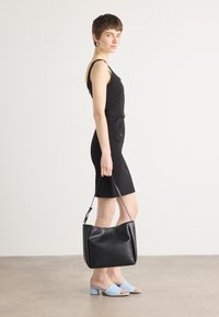 Svart bodycon-kjole med justerbare stropper, med to frontknapper. Svart skinn skulderveske, blå mules med firkantet tå og blokkhel.