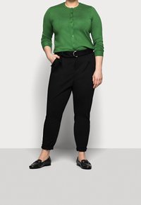 Groen vest met knopen gecombineerd met zwarte, taillehoge broek. Model draagt zwarte loafers, die een gladde textuur en een getailleerd ontwerp tonen.