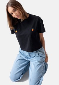 Czarny bawełniany t-shirt z krótkim rękawem z dwoma haftowanymi wzorami pomarańczy. Połączony z jasnoniebieskimi, luźnymi dżinsami.