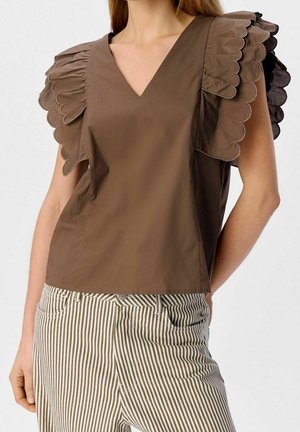 Brown sleeveless top with ruffled scalloped shoulder details paired with high-waisted green and white vertical striped pants.