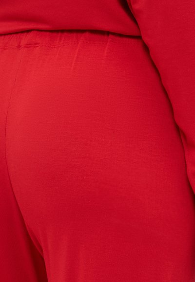 Red fitted garment, smooth texture, elastic waistband, minimal seams, emphasizes shape. Displays solid color with no visible patterns or accents.
