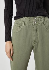 Pantalones de algodón verdes con un corte relajado, que cuentan con dos bolsillos frontales y cierre de doble botón en la cintura. Textura suave y costuras visibles.