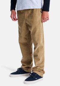 Katoenen ribbroeken in beige, met een rechte pasvorm en verticale ribbelstructuur. Gecombineerd met donkerblauwe suède sneakers.