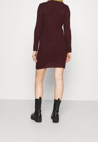 Burgundy ribbed knit dress with long sleeves, featuring a mid-thigh length and slight side slits, paired with black ankle boots.
