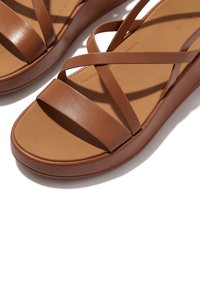 Bruine leren sandalen met kruislings gespen en een dikke, stevige platformzool. Gladde textuur, minimalistisch design en neutraal kleurenschema.