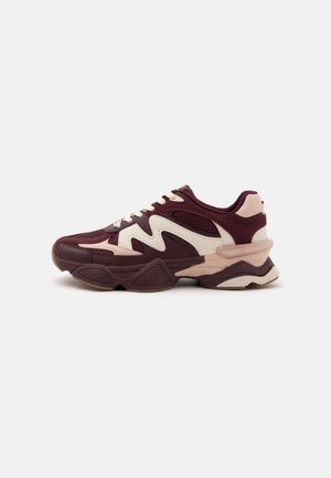 Mørkerød og beige atletiksneakers med mesh- og ruskindspaneler, hvide snørebånd og en tyk, tekstureret sål set fra siden.