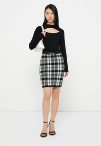 Top preto de manga comprida com um recorte, combinado com uma minissaia xadrez justa em preto, branco e cinza, com um detalhe de cinto. Saltos pretos com tiras.