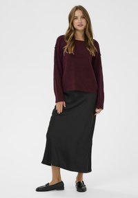 Bordeaux striktrøje med lange ærmer, parret med en sort glat maxi-nederdel og sorte loafers, hvilket skaber et lagdelt outfit.