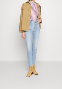 Person wearing light blue high-waist button-fly jeans, striped red and blue t-shirt, tan jacket draped over shoulders, and tan suede ankle boots.