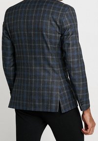 Maßgeschneiderte graue Blazer mit blauem Karomuster, zwei Rückenbelüftungen und knöpfbaren Ärmeln. Hergestellt aus strukturiertem Stoff für einen formellen Look.