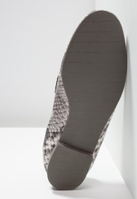 Semelle d'une chaussure au motif de peau de serpent, avec la marque "Kennel & Schmenger" estampillée sur le fond en caoutchouc noir.