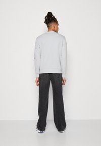 Felpa grigia chiara con polsini e orlo a costine, abbinata a jeans neri a vestibilità ampia. I jeans presentano un classico design a cinque tasche.