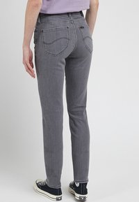 Grå denimbyxor med smal passform, med kontrasterande vit sömnad och två bakfickor. Bärs med svarta kanvas sneakers.