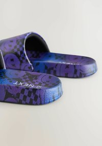 Lila och blåa halkskyddsandaler med en texturerad design och rutiga samt grafiska mönster. Platt sula och bred rem med rundade kanter.