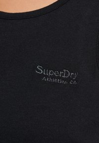 Černý top bez rukávů s kulatým výstřihem a jemnou texturou, na hrudi vyšitým logem "SuperDry" v stříbrné barvě.