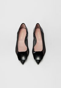 Ballerines noires à bout pointu avec un accent carré brillant, côtés transparents, texture en cuir lisse et intérieur rose doux.