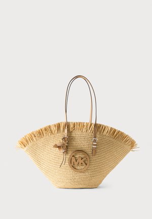 Sac cabas en paille tissée avec bord supérieur à franges, poignées en cuir marron clair et logo circulaire MK sur le devant avec accent gland en cuir.