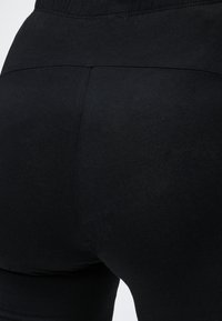 Gros plan sur un legging noir ajusté en tissu montrant les détails des coutures à la taille et au niveau des fesses.