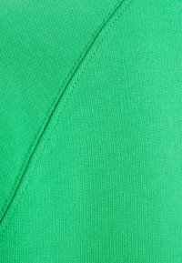 Tejido verde con una textura suave y un tejido uniforme, con un detalle de costura diagonal que realza el diseño.