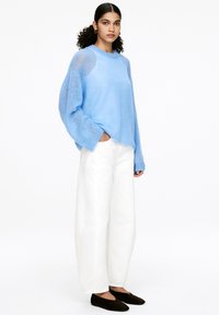 Hellblauer Strickpullover mit strukturierten Schultern, kombiniert mit weiten weißen Hosen und dunklen flachen Schuhen. Lässige und entspannte Passform.