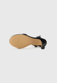 Escarpin noir avec une tige en cuir lisse, une semelle en vinyle à texture nervurée et un talon courbé et mince pour le soutien.