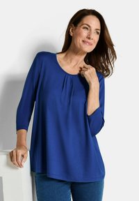 Königsblaues Langarmshirt mit rundem Ausschnitt und Faltendetails. Weiches Material und lockere Passform, kombiniert mit Denim-Jeans.