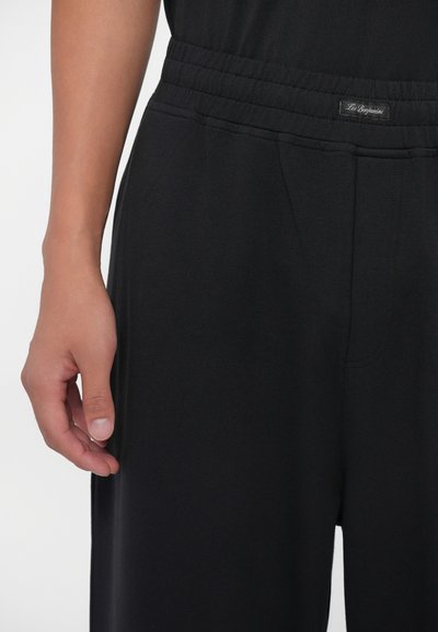 Pantalones deportivos negros con una cinturilla elástica, que cuentan con una pequeña etiqueta de logo. La tela parece suave y lisa con un diseño de pierna recta.