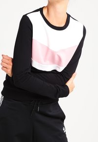 Svart sweatshirt med en vit och ljusrosa horisontell färgblockering framtill. Har långa ärmar och rund halsringning. Mjuk textur.