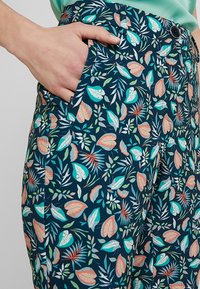 Navy trousers with a leafy pattern in teal, orange, and green. Features a side pocket and a smooth, lightweight fabric.