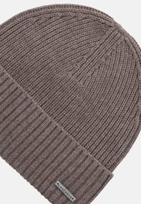 Brązowa dziana czapka beanie z pionowym prążkowaniem i podwijanym mankietem. Ma małą prostokątną metkę z tkaniny z napisem na mankiecie.