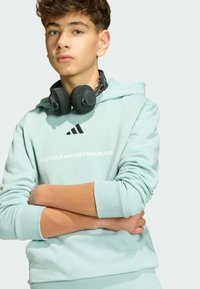 Svetlo mentolová mikina s kangaroo vreckom, so bielym logom "ADIDAS SPORTSWEAR" a čiernymi tromi pruhmi. Slúchadlá ležia na krku.