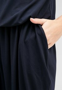 Marinblå plagg med en mjuk textur, utrustad med en sidoficka och lös passform, som faller runt midjan och höftområdet.