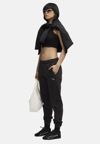 Čierna skrátená tielko, čierne tepláky s elastickým pásom, biele logo Puma, čierne tenisky, slnečné okuliare a biela kabelka.