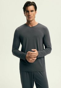 Szary longsleeve z dekoltem w serek, wykonany z miękkiego materiału. Koszula zestawiona jest z dopasowanymi szarymi spodniami.
