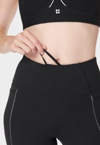 Zwarte sportbeha met een strakke pasvorm, voorzien van een klein logo en bandjes die zijn gestopt in hoge zwarte leggings met contrasterende stiksels.