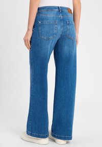 Brede denim jeans in een middelblauwe wassing, met een klassieke vijf-pocket ontwerp en een bruine leren merkpatch op de taille.