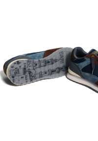 Zapatillas con una mezcla de gamuza y cuero en tonos azul, marrón y gris. La suela gruesa y texturizada presenta un diseño detallado. Punta redondeada y diseño con cordones.