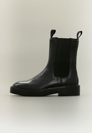 Black leather Chelsea boot with elastic side panels, pull tabs on front and back, and a thick sole on a neutral background.
