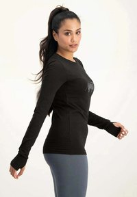Schwarzes Langarmshirt mit rundem Ausschnitt, mit enganliegenden Ärmeln und Daumenlöchern, getragen mit hellblauen Leggings.