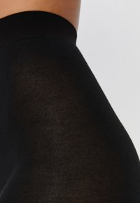 Nieprzezroczyste czarne legginsy o miękkiej teksturze i szerokim elastycznym pasku w talii, charakteryzujące się gładkim wykończeniem oraz dopasowanym krojem.