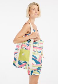 Grote tote bag van gestippeld stof met roze, groen en blauwe abstracte ontwerpen, voorzien van crèmekleurige schouderbanden en een groene voorkantzak.