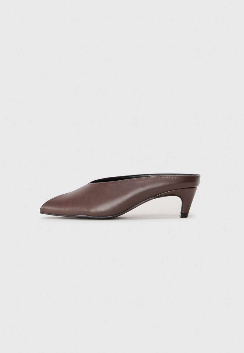 Mules en cuir marron avec un bout pointu, un talon bas et une texture lisse. Design à dos ouvert, silhouette élégante et style minimaliste.