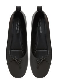 Ballerine in pelle nera con punta tonda, suola piatta e dettaglio a fiocco decorativo sulla parte frontale. Texture liscia e design minimalista.